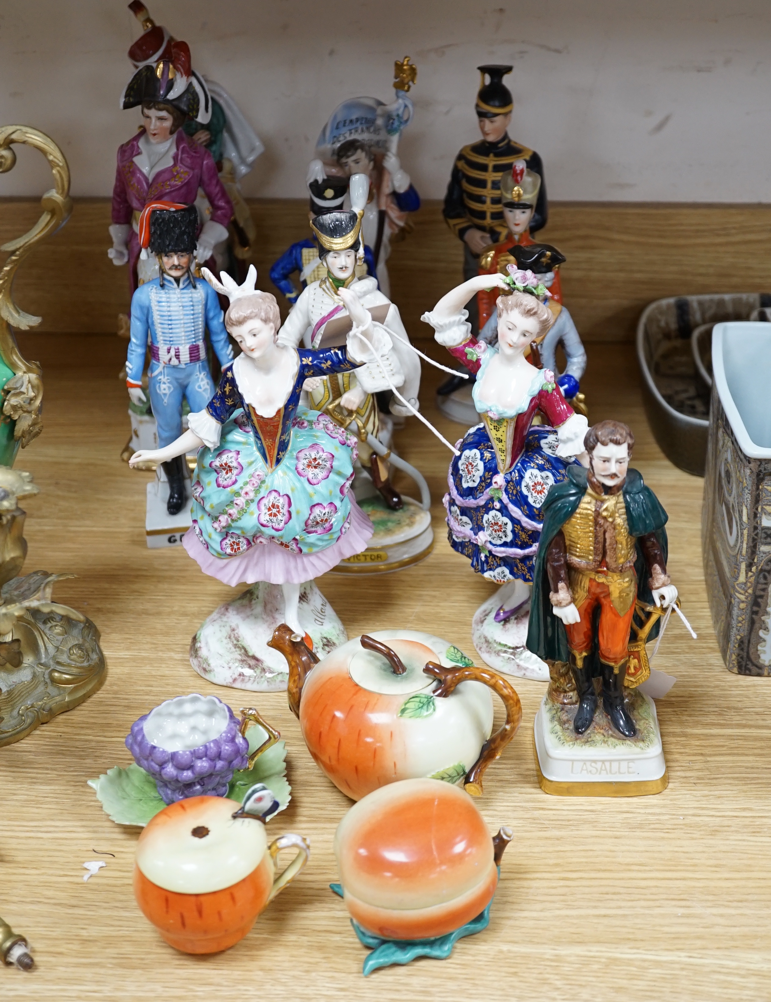 A group of Continental porcelain military figures, two porcelain figures of dancing females and four pieces of tableware in the form of fruit